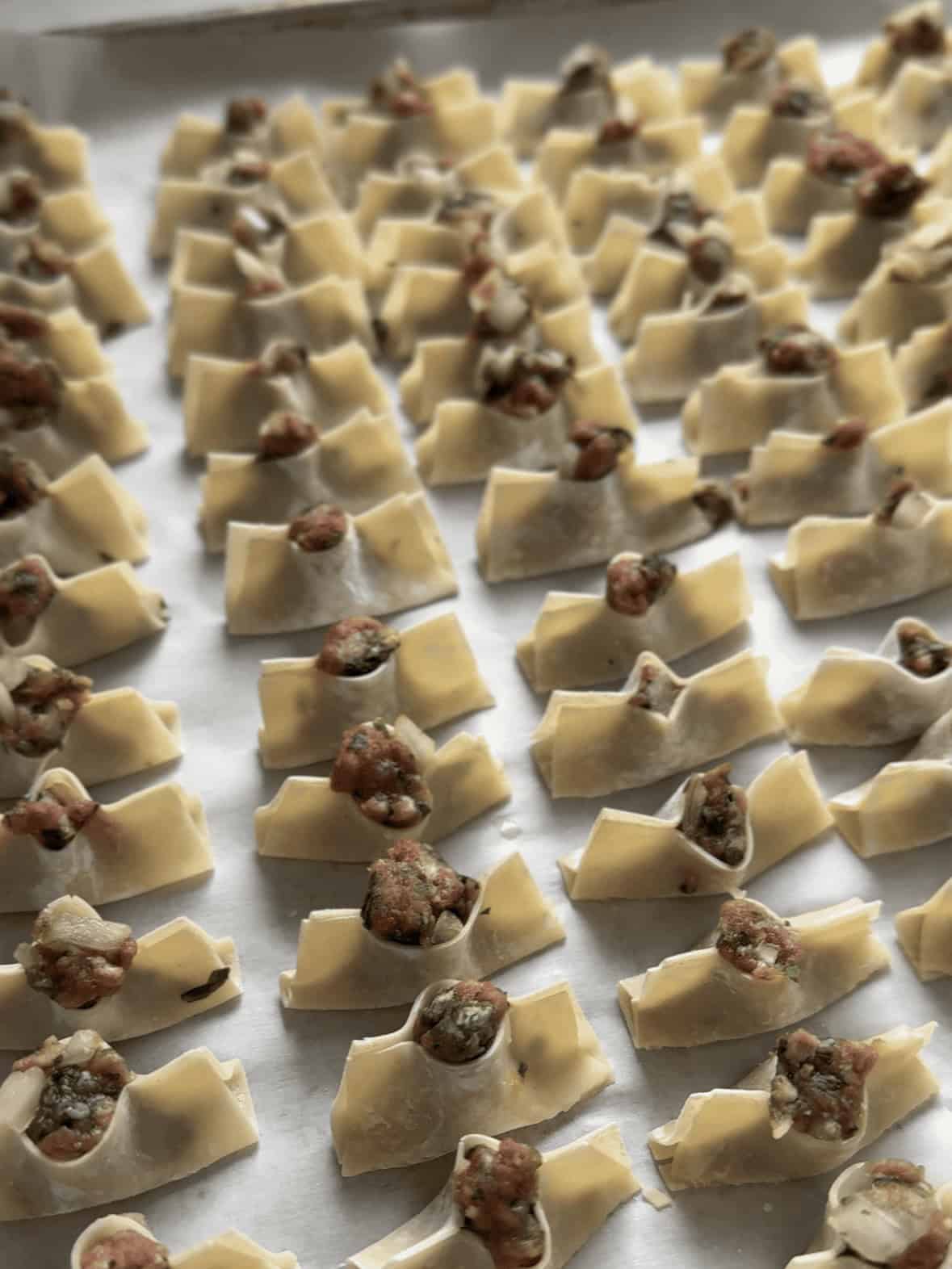 Unbaked Armenian Manti boats lined on a parchment paper baking tray before going into the oven.