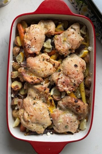 Overhead view of one pan chicken thighs and veggies with baby potatoes, rainbow carrots, red onion, lemon, thyme, and feta