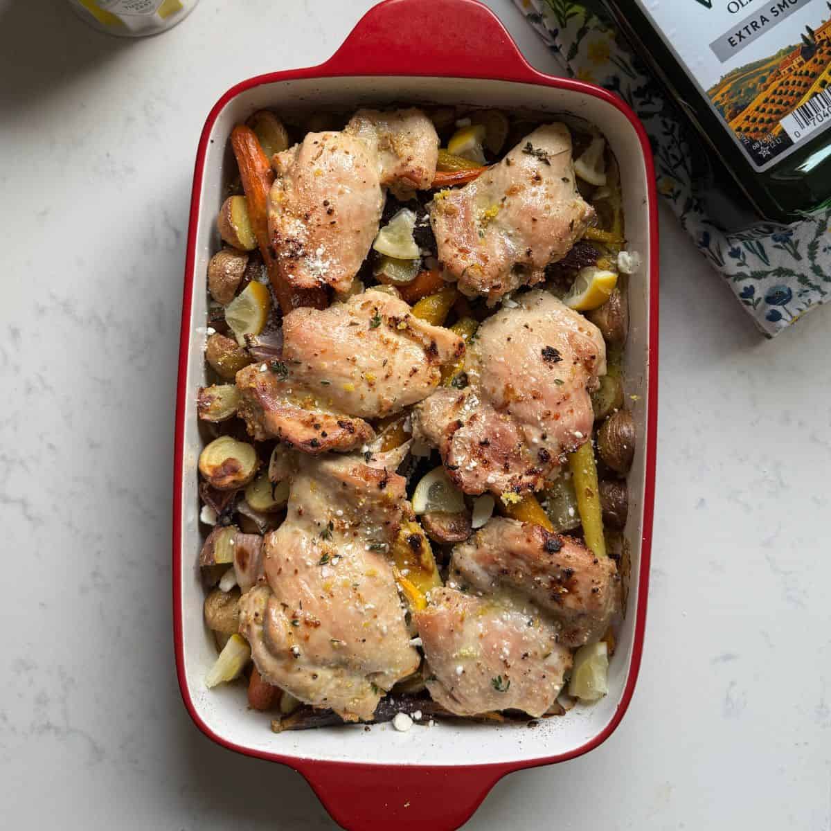 Overhead view of one pan chicken thighs and veggies with baby potatoes, rainbow carrots, red onion, lemon, thyme, and feta