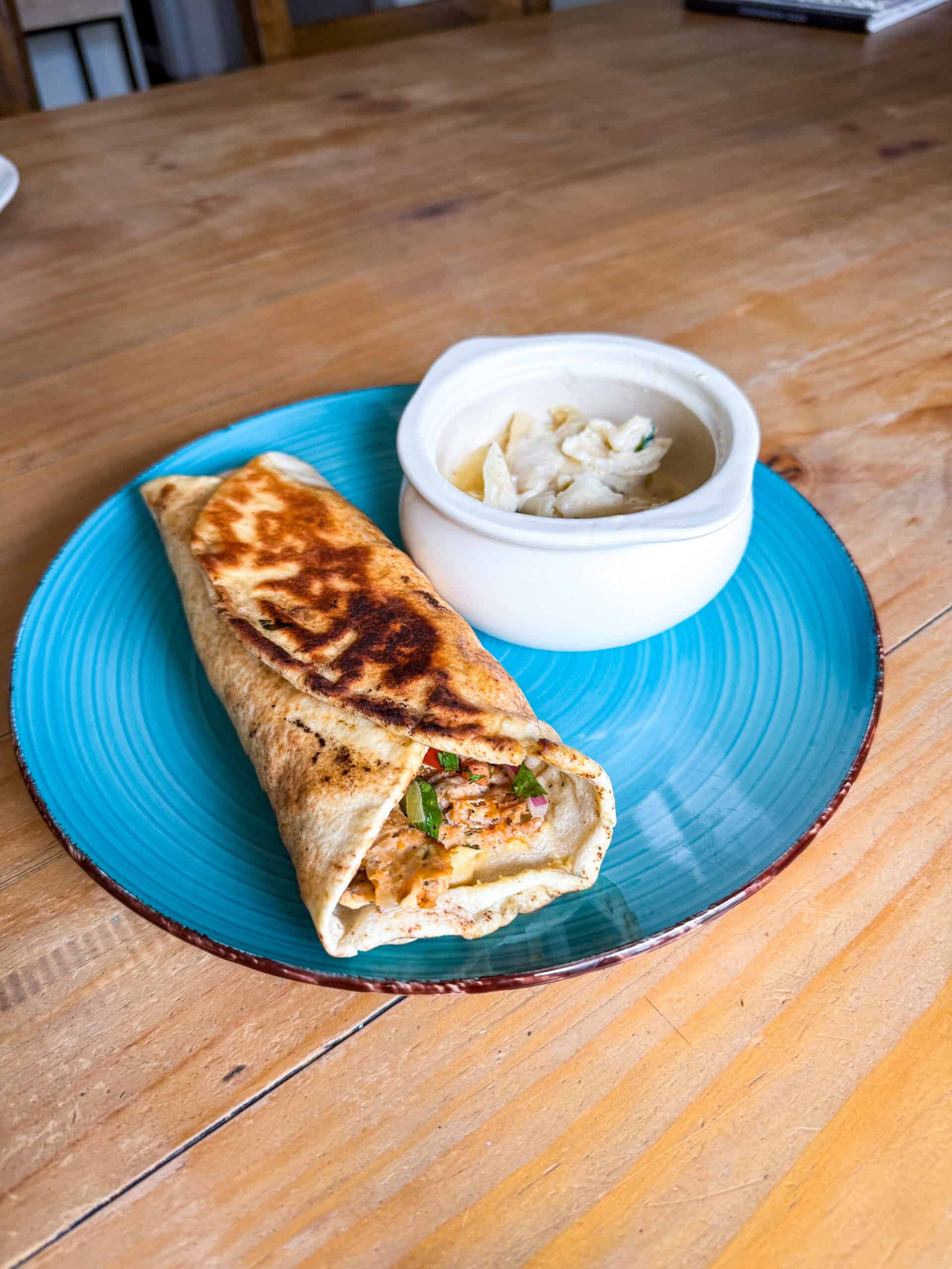 Golden pan-fried chicken doner kabob wrap on a teal blue plate served with a side of hummus on a rustic wood table
