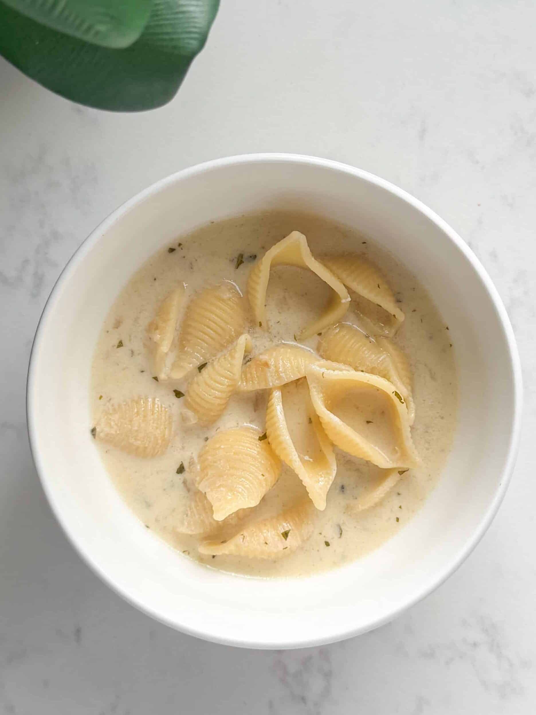 Overhead view of a bowl of Armenian yogurt soup with shell pasta, garnished with dried mint and a drizzle of olive oil on a warm surface