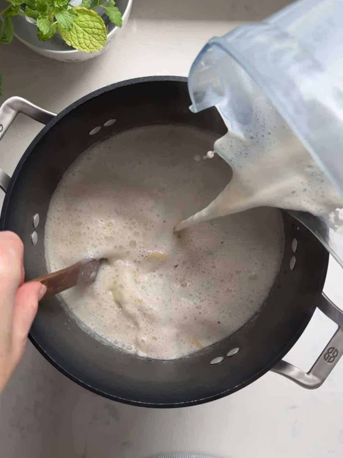 Yogurt and egg mixture being slowly poured into the pot of Armenian yogurt soup while being stirred constantly with a wooden spoon