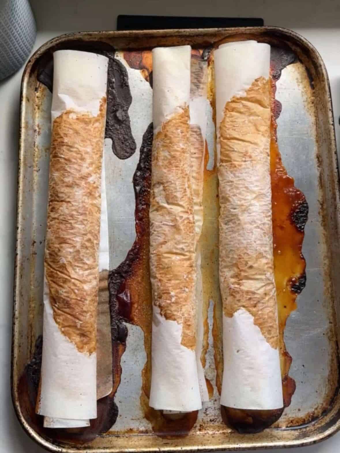 Three chicken doner kabob rolls wrapped in parchment paper on a baking sheet ready to go into a 400 degree oven