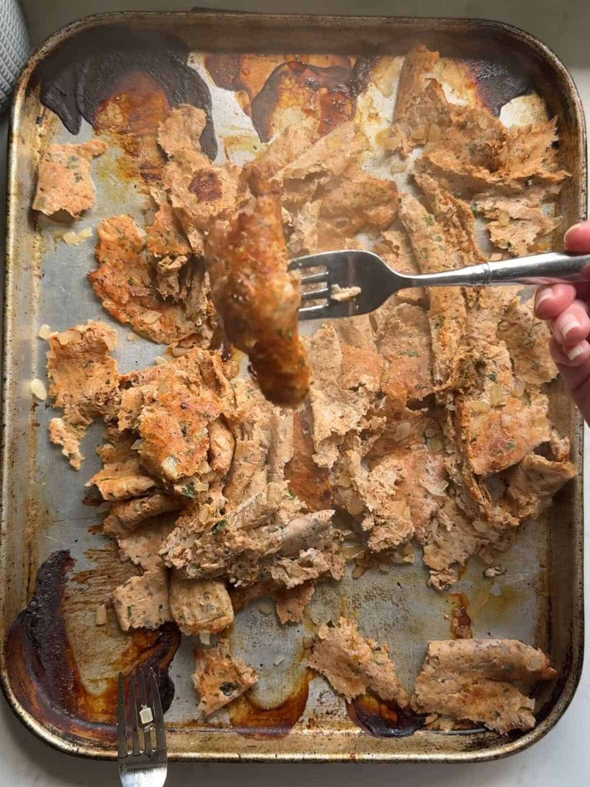 Broken up ground chicken doner kabob pieces on a baking sheet after broiling showing golden crispy edges from the oven method