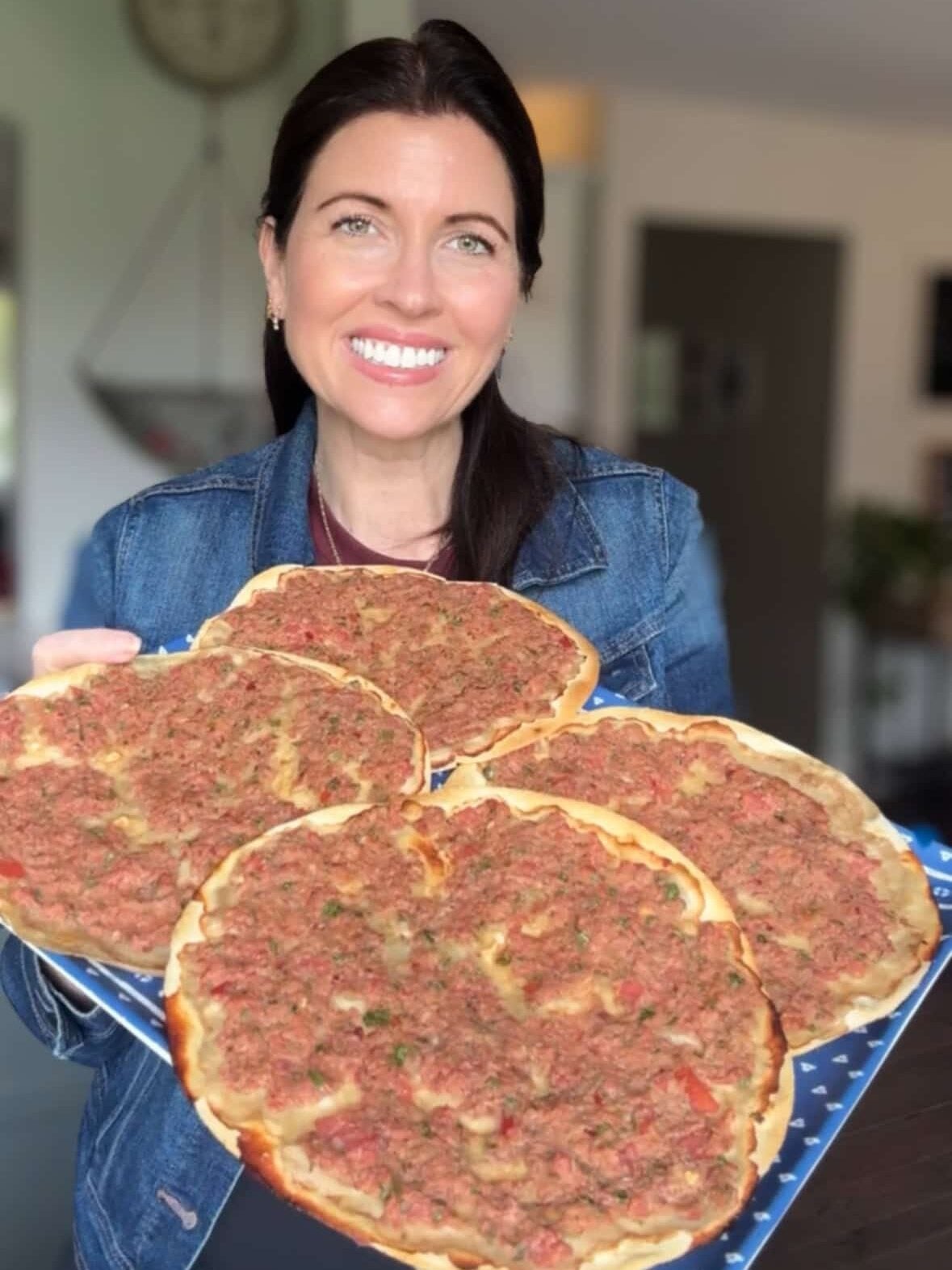Hands holding a tray of freshly baked Armenian lahmajoun ready to serve.