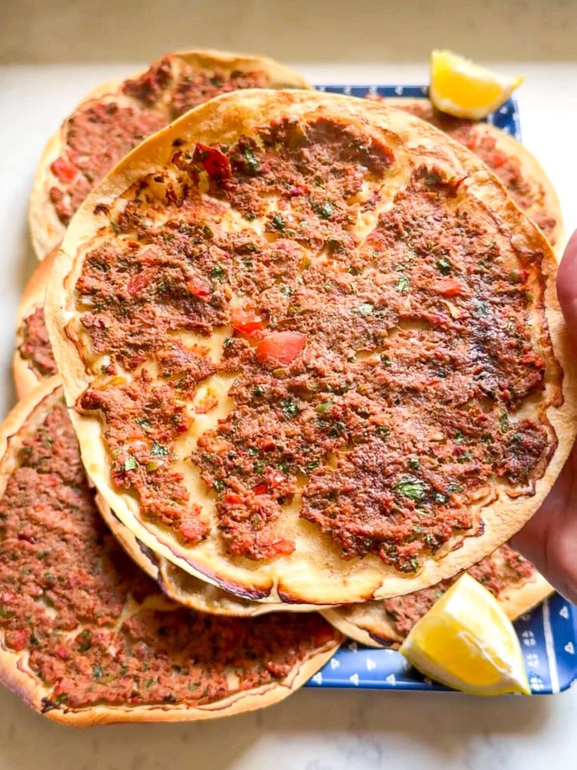 Hands holding a single piece of Armenian lahmajoun up close showing the thin crispy crust and spiced ground meat topping.