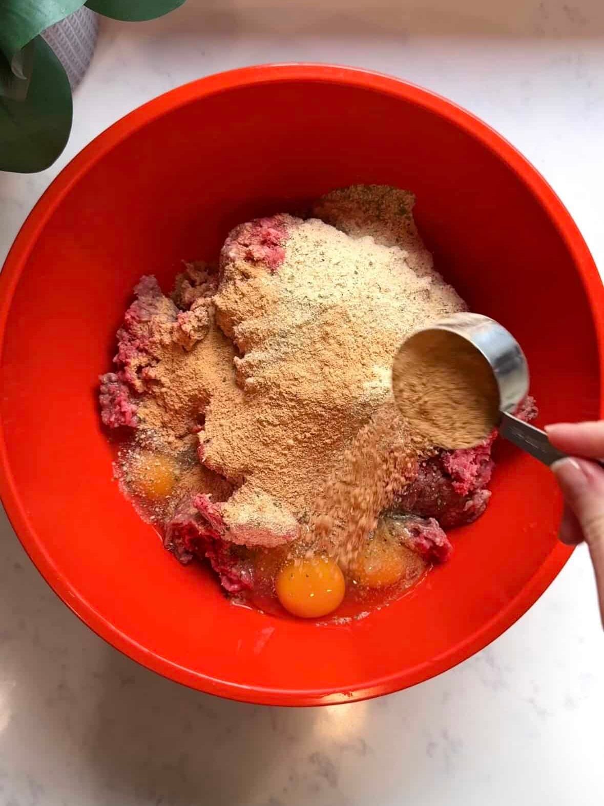 Red mixing bowl with ground sirloin egg and breadcrumbs being combined to make sujakaki soutzoukakia Smyrna meatball mixture