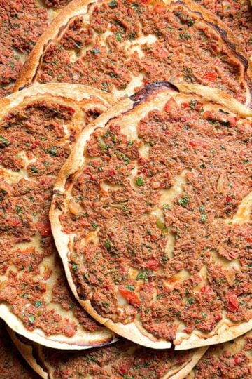 Overhead flat lay of multiple crispy Armenian lahmajoun arranged on a serving tray showing the golden baked meat topping and thin crust.