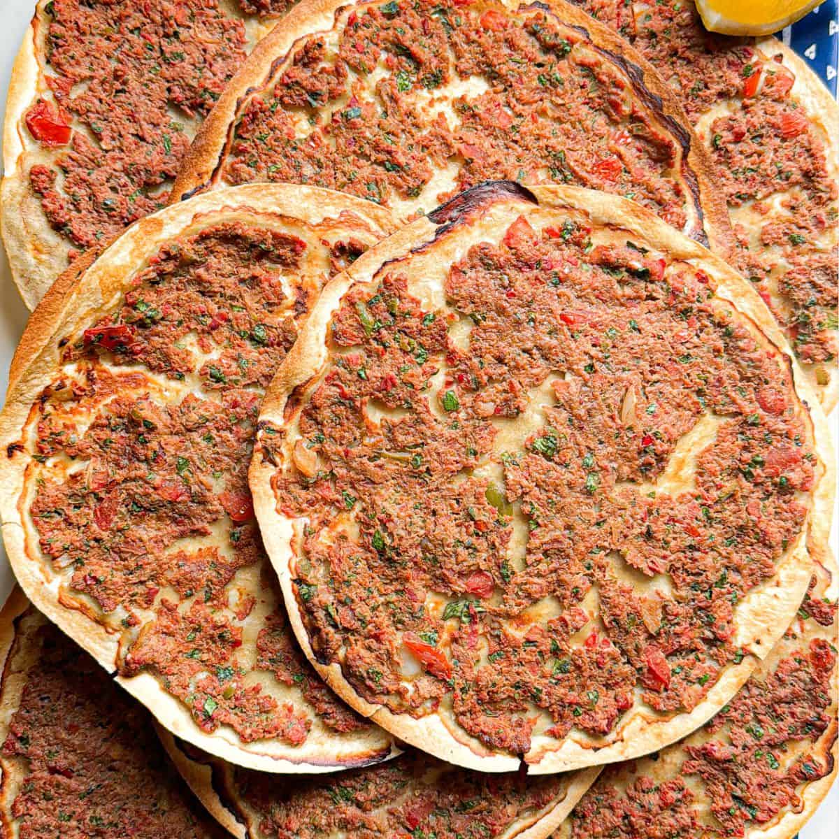 Overhead flat lay of multiple crispy Armenian lahmajoun arranged on a serving tray showing the golden baked meat topping and thin crust.