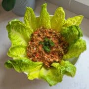 Overhead view of Armenian eech red tabouli in a white bowl surrounded by romaine lettuce leaves on a marble countertop