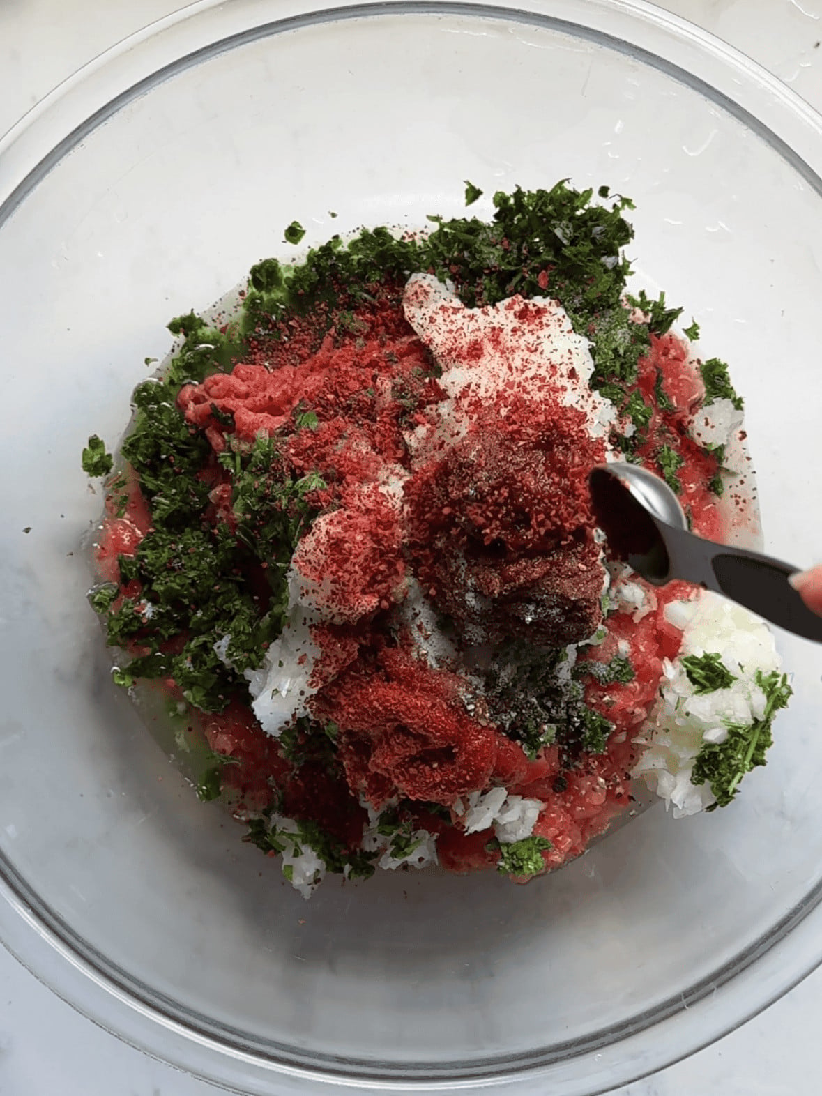 Large mixing bowl with combined ground beef, processed vegetables, garlic, red pepper paste, tomato paste, and Armenian spices mixed together by hand