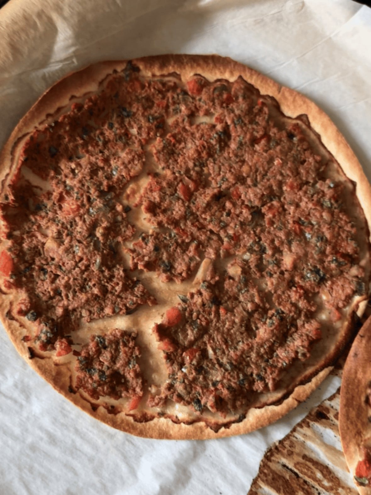 Golden crispy Armenian lahmajoun fresh out of the oven on a parchment-lined baking sheet with charred edges.