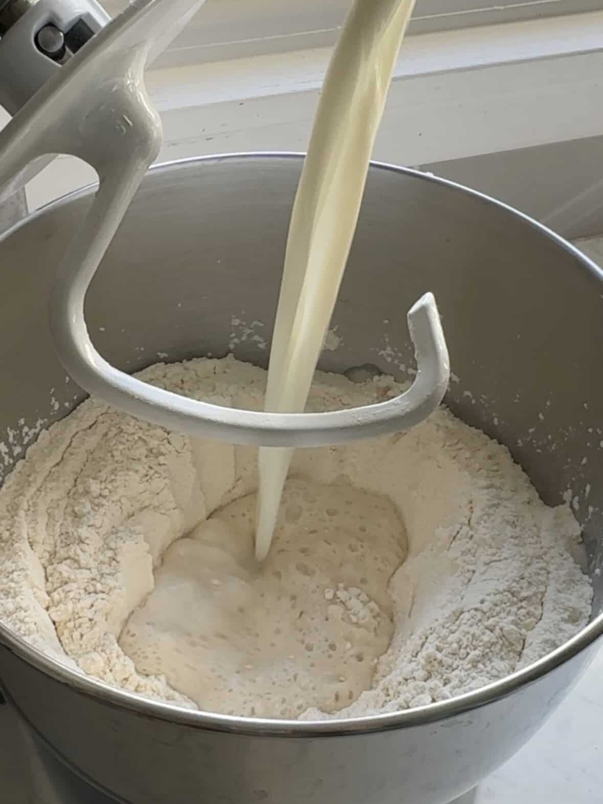 Wet ingredients pouring into a stand mixer bowl with flour for Armenian cheoreg dough