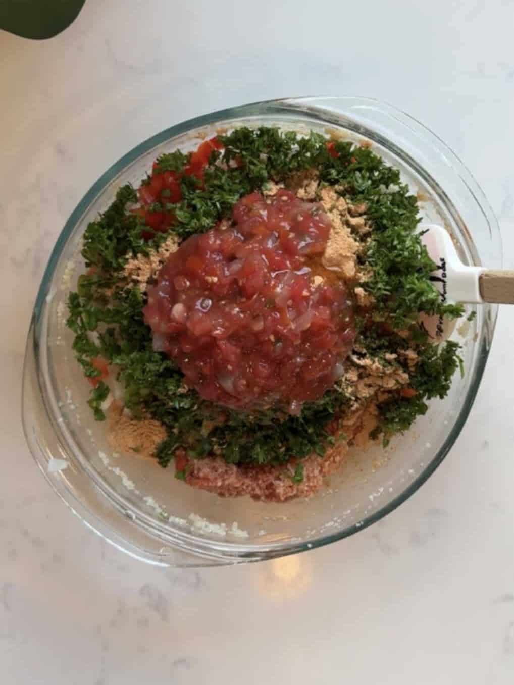 Glass bowl with bloomed bulgur, fresh parsley, chopped vegetables and chunky salsa before mixing for Armenian eech red tabouli