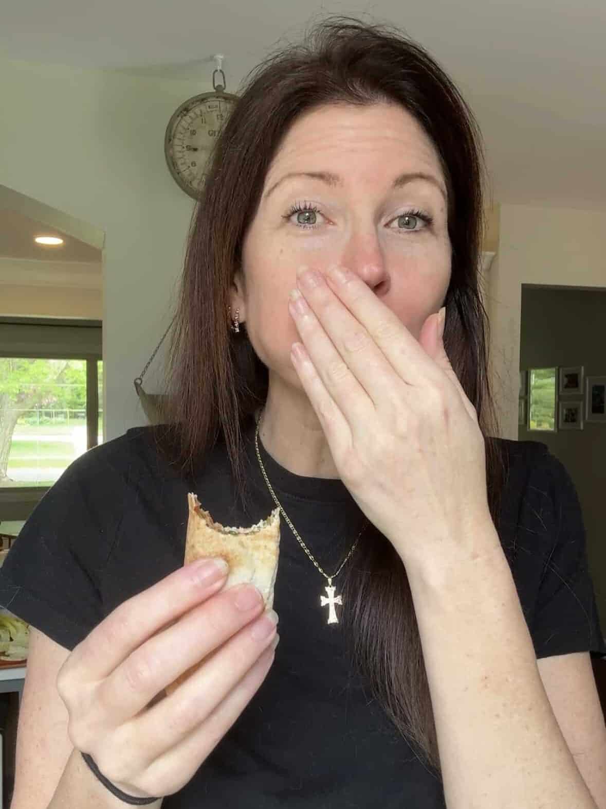 Woman holding flat pita with Armenian eech red tabouli with hand over mouth mid-bite