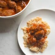 Overhead view of sujakaki soutzoukakia Smyrna meatballs in tomato sauce served over rice pilaf on a white plate with serving bowl on white marble surface