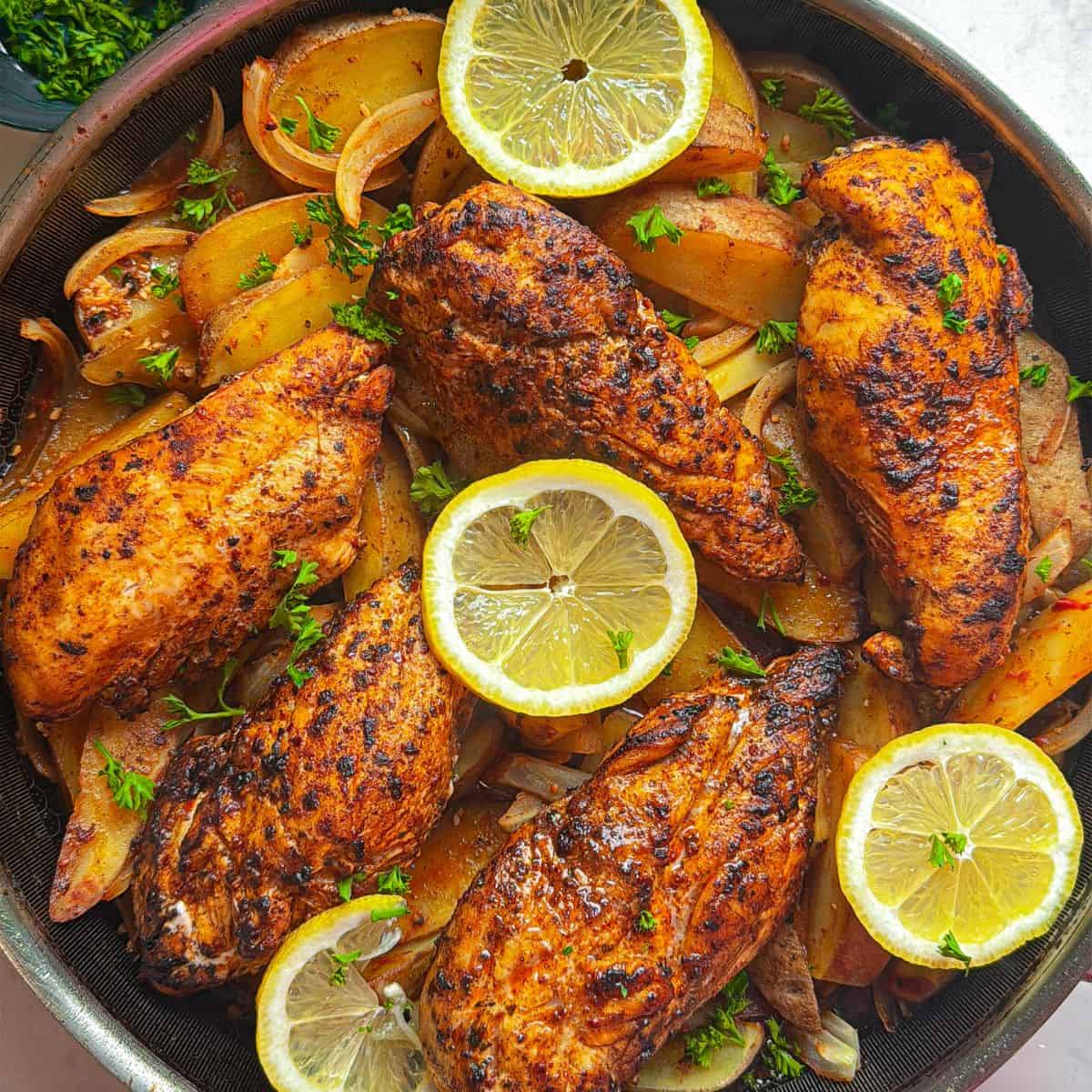 Overhead view of Aleppo pepper chicken breasts and potatoes in a dark skillet garnished with lemon slices and fresh parsley