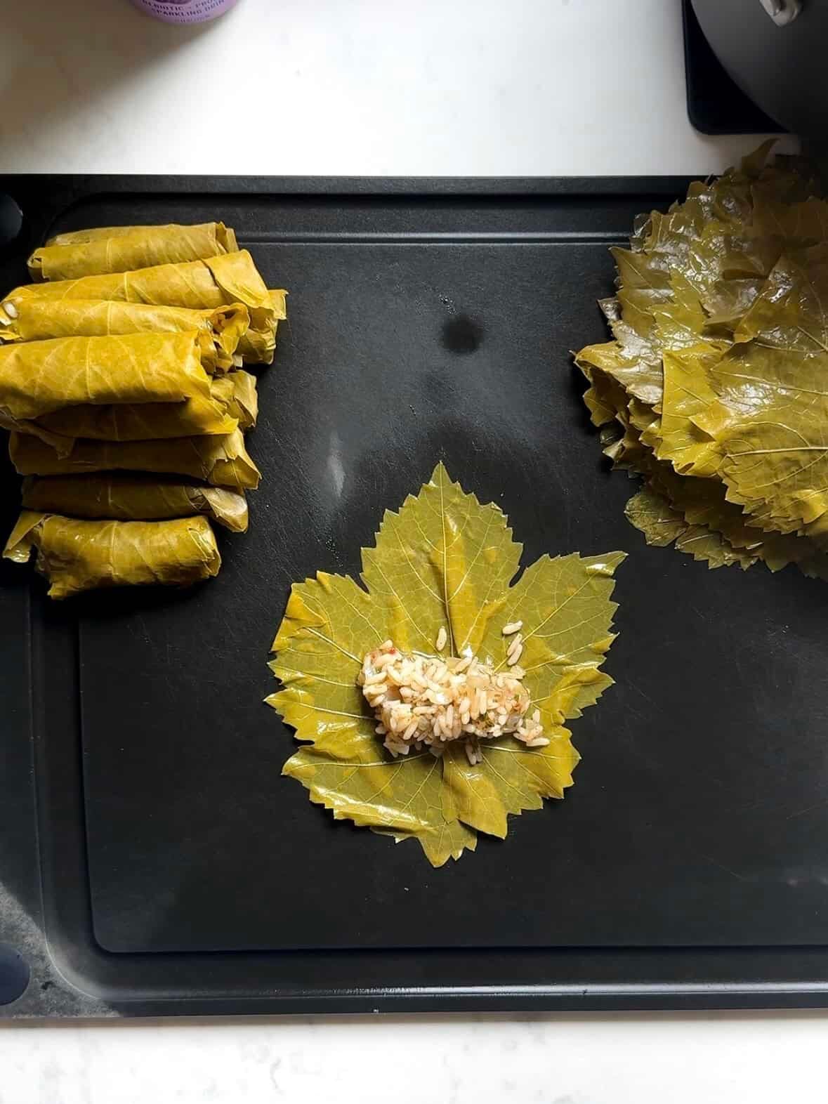 Grape leaf laid flat with a spoonful of rice filling near the stem end