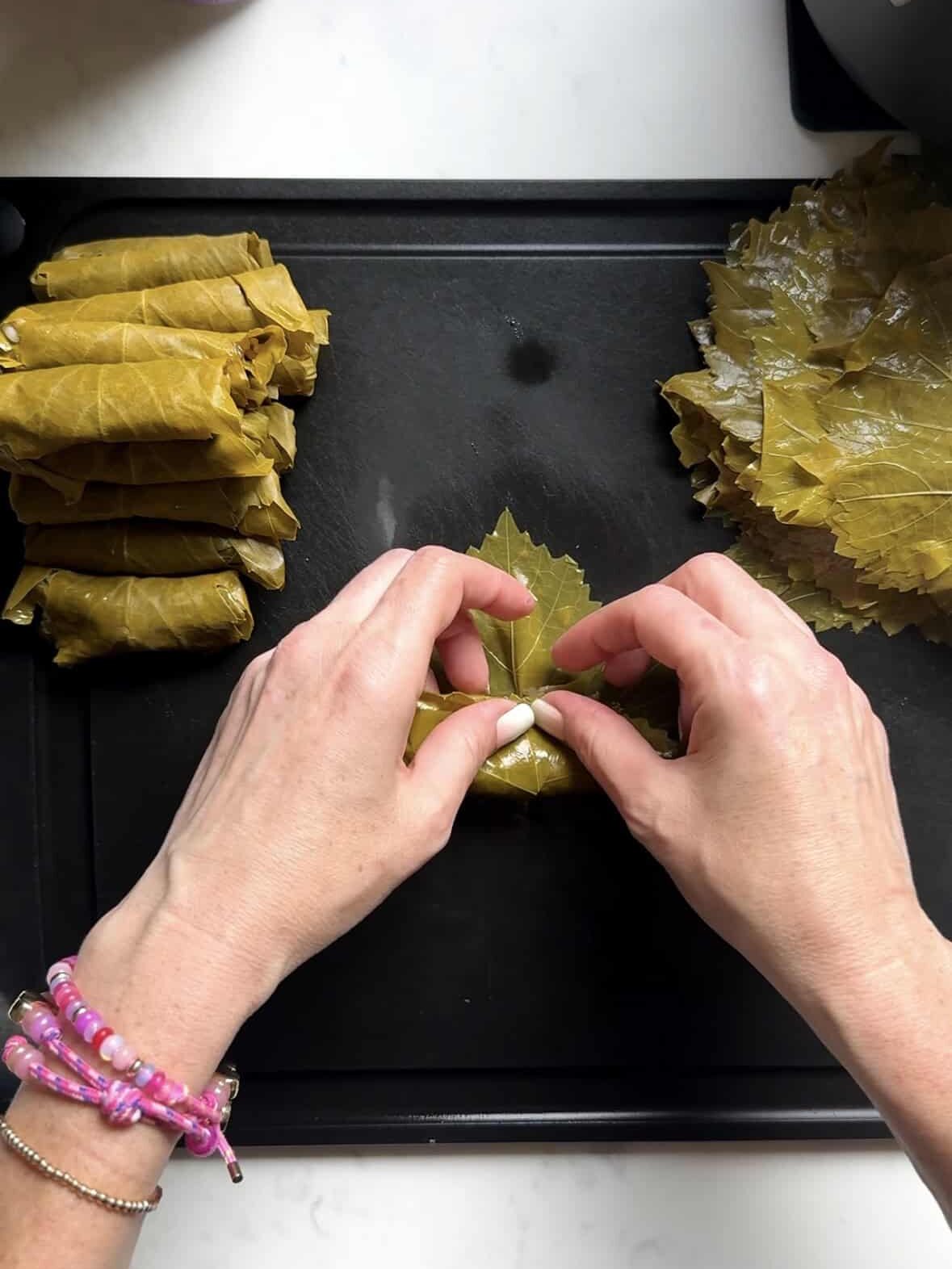Hands folding the stem end of a grape leaf up over the filling