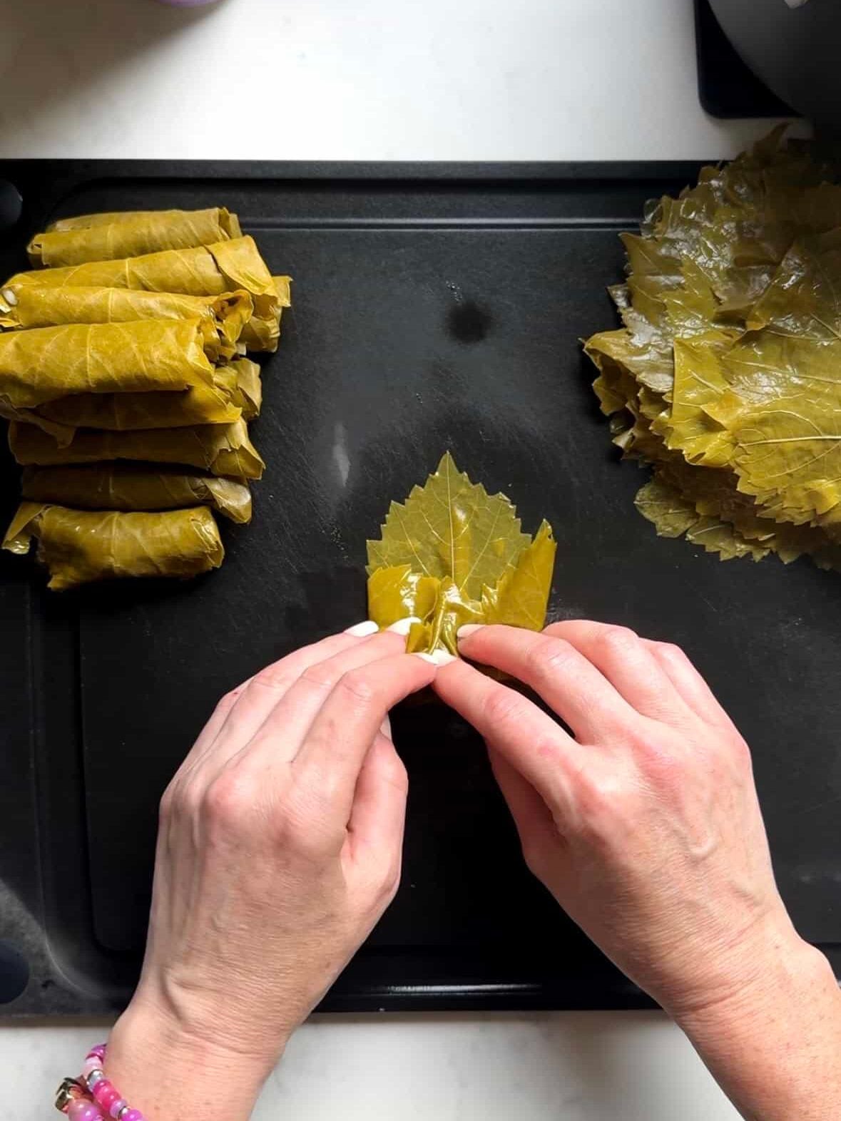 Hands folding the sides of a grape leaf inward around the filling