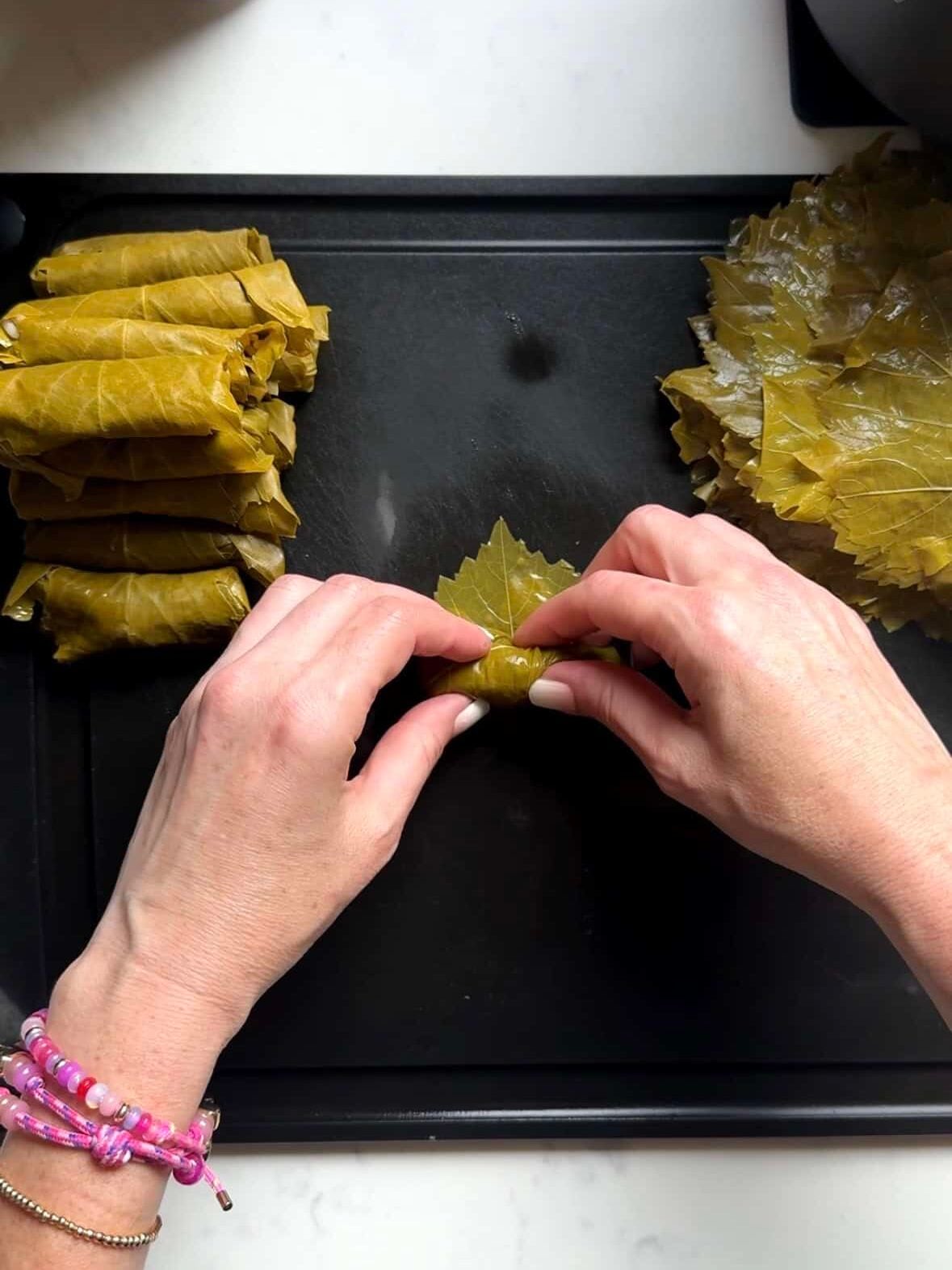 Hands rolling a grape leaf into a log around the rice filling
