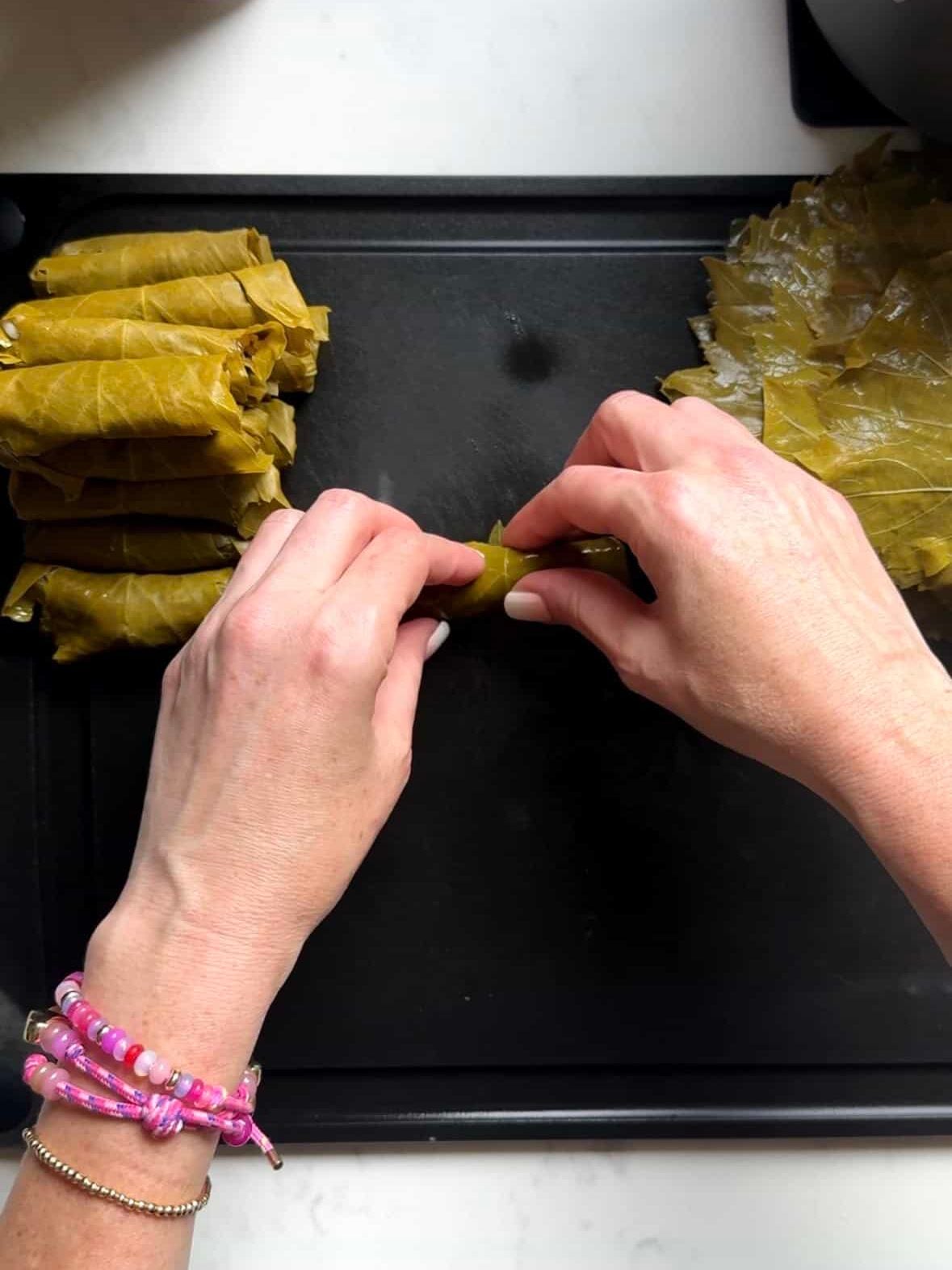 Hands finishing rolling a stuffed grape leaf into a tight cylinder
