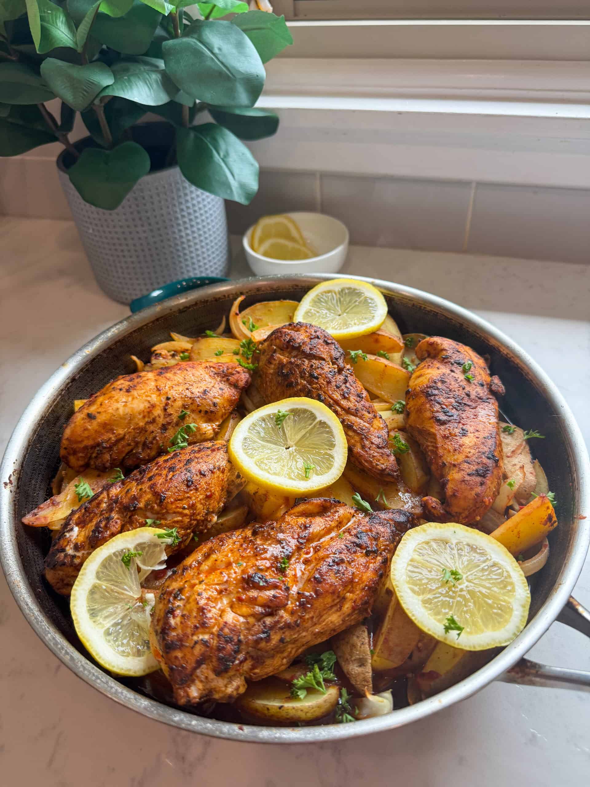 One pot Aleppo pepper chicken and potatoes in a silver skillet near a window with a green plant in the background