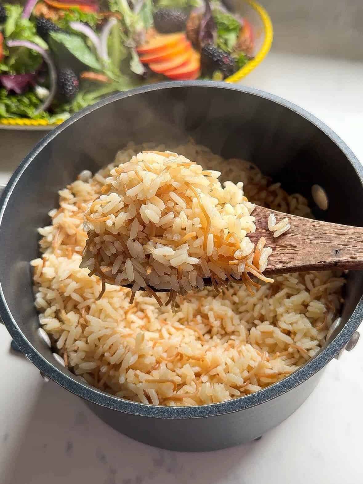 Close-up of a wooden spoon lifting fluffy Armenian rice pilaf with golden toasted noodles out of the pot