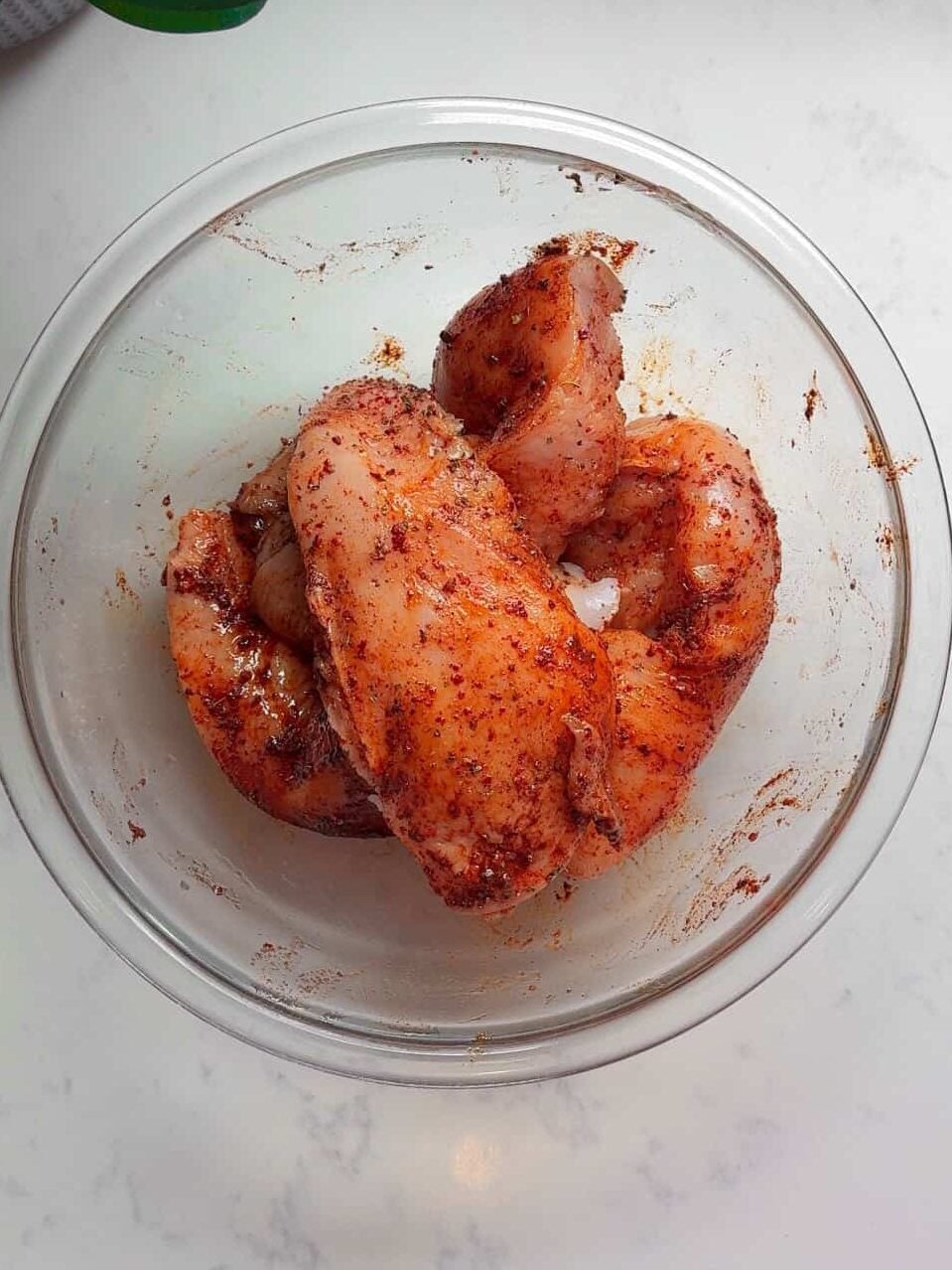 Raw chicken breasts coated in Aleppo pepper spice blend in a glass mixing bowl