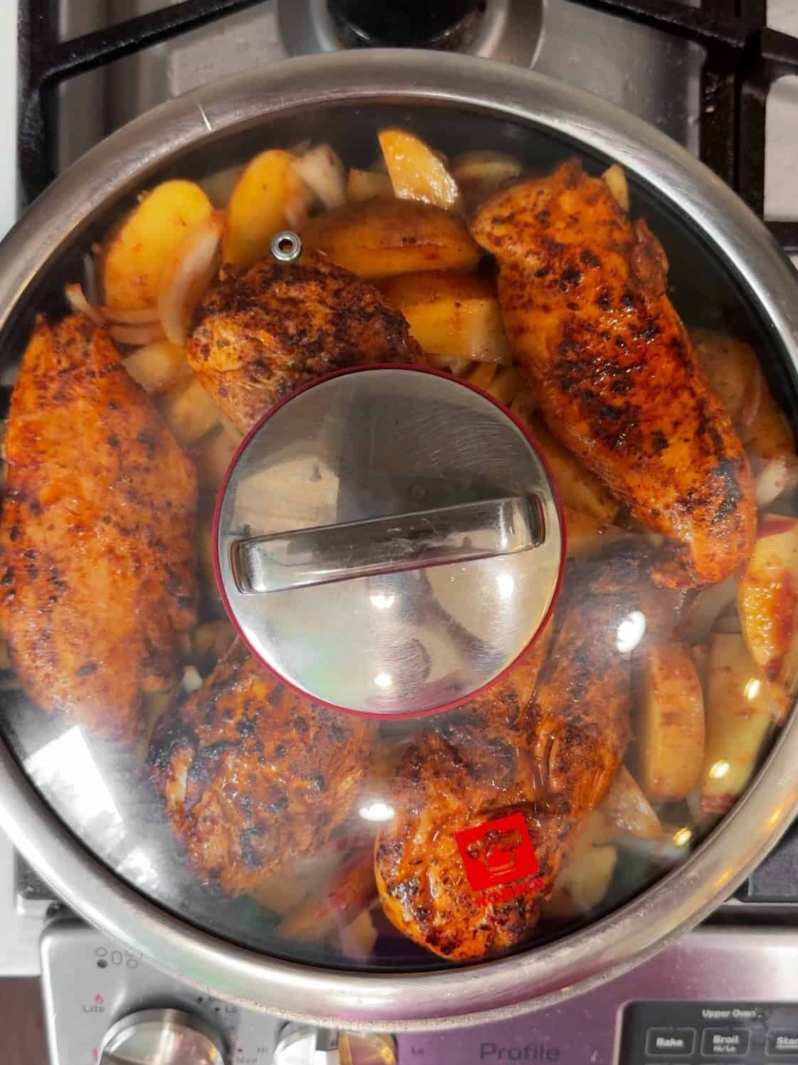 Aleppo pepper chicken breasts and potatoes cooking covered in a large skillet on a gas stovetop