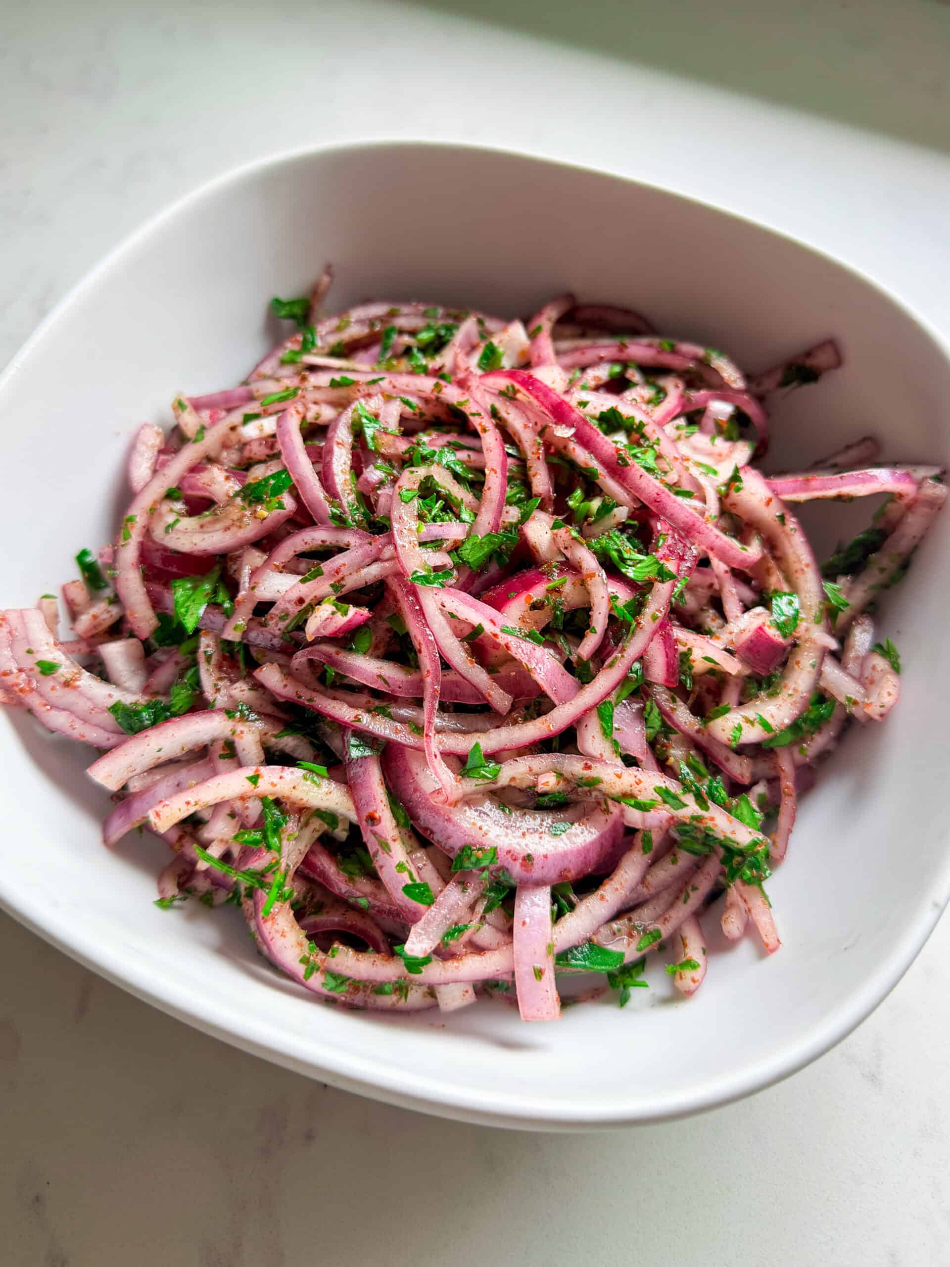 Close-up of sumac onion salad with parsley and olive oil in a white bowl