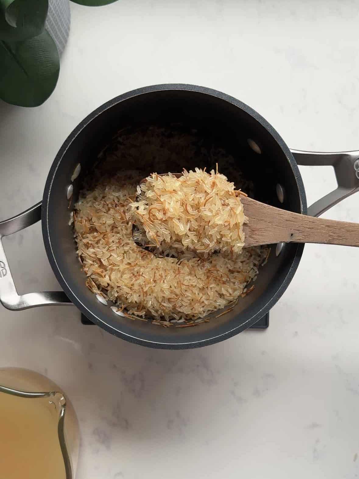Long-grain white rice added to toasted golden noodles in a pot, toasted together for Armenian rice pilaf