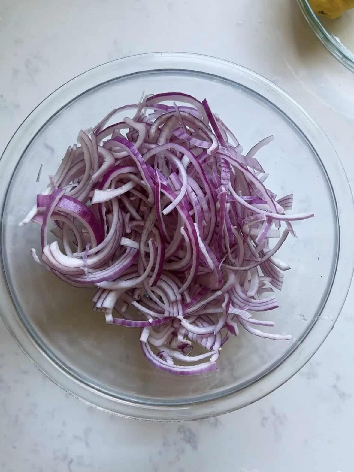Thinly sliced red onions in a glass bowl before being tossed with sumac