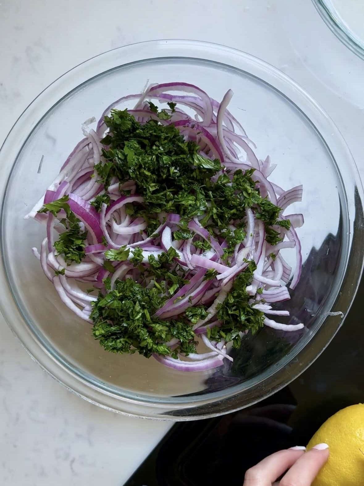 Sliced red onions topped with fresh chopped parsley in a glass mixing bowl