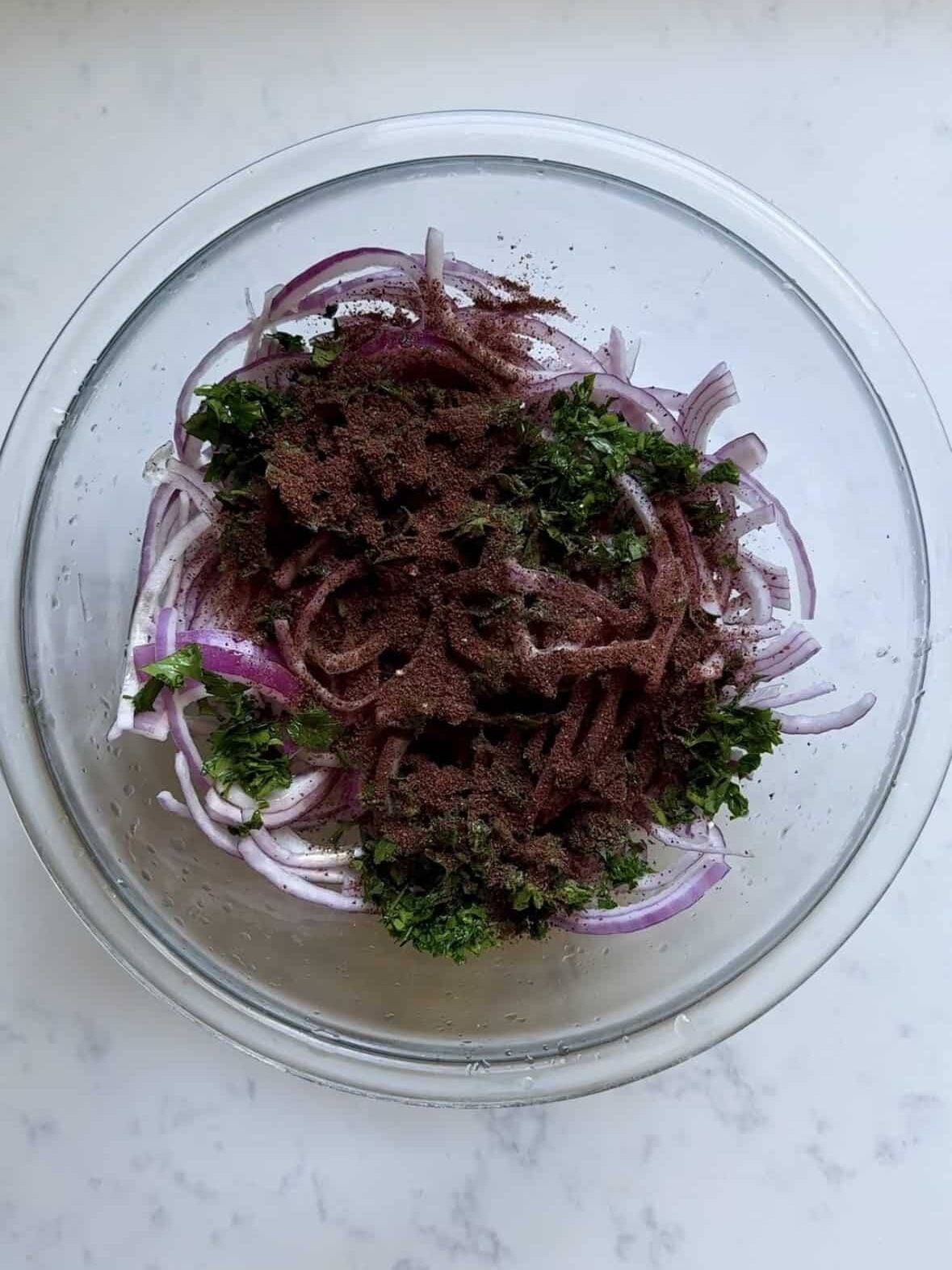 Ground sumac spice sprinkled over sliced onions and parsley before mixing