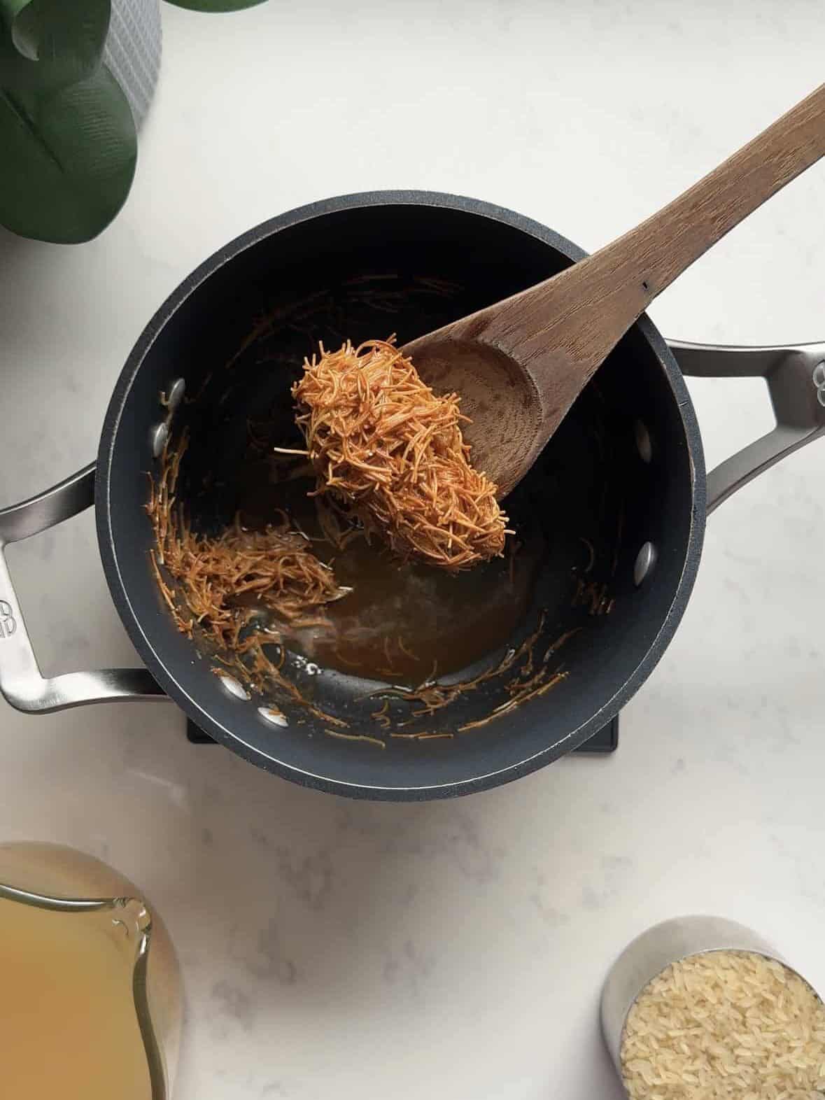 Fine vermicelli toasted golden brown in butter on a wooden spoon, the first step of making Armenian rice pilaf