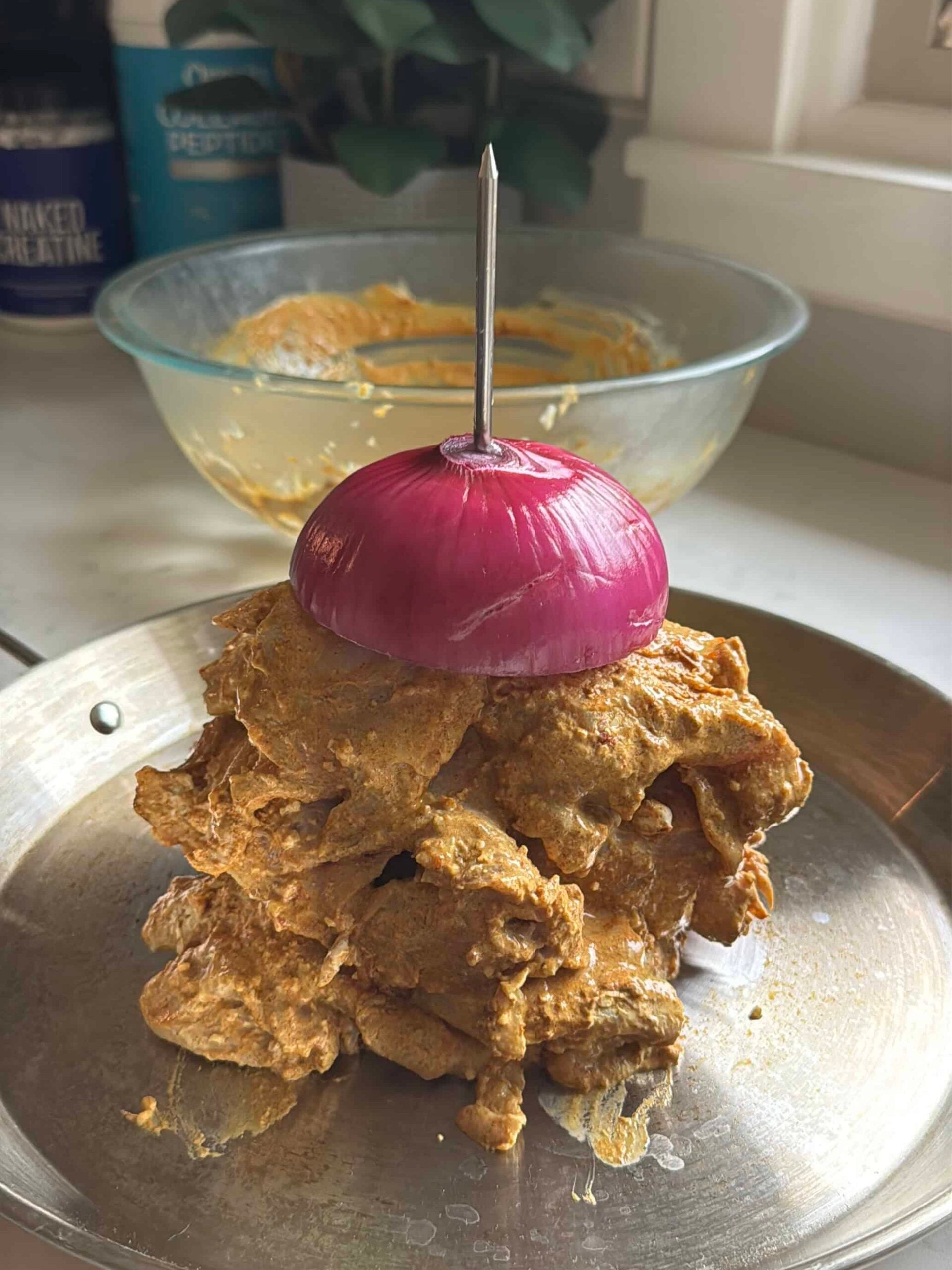 Marinated chicken stacked on a vertical spit with a red onion on top, ready to go in the oven