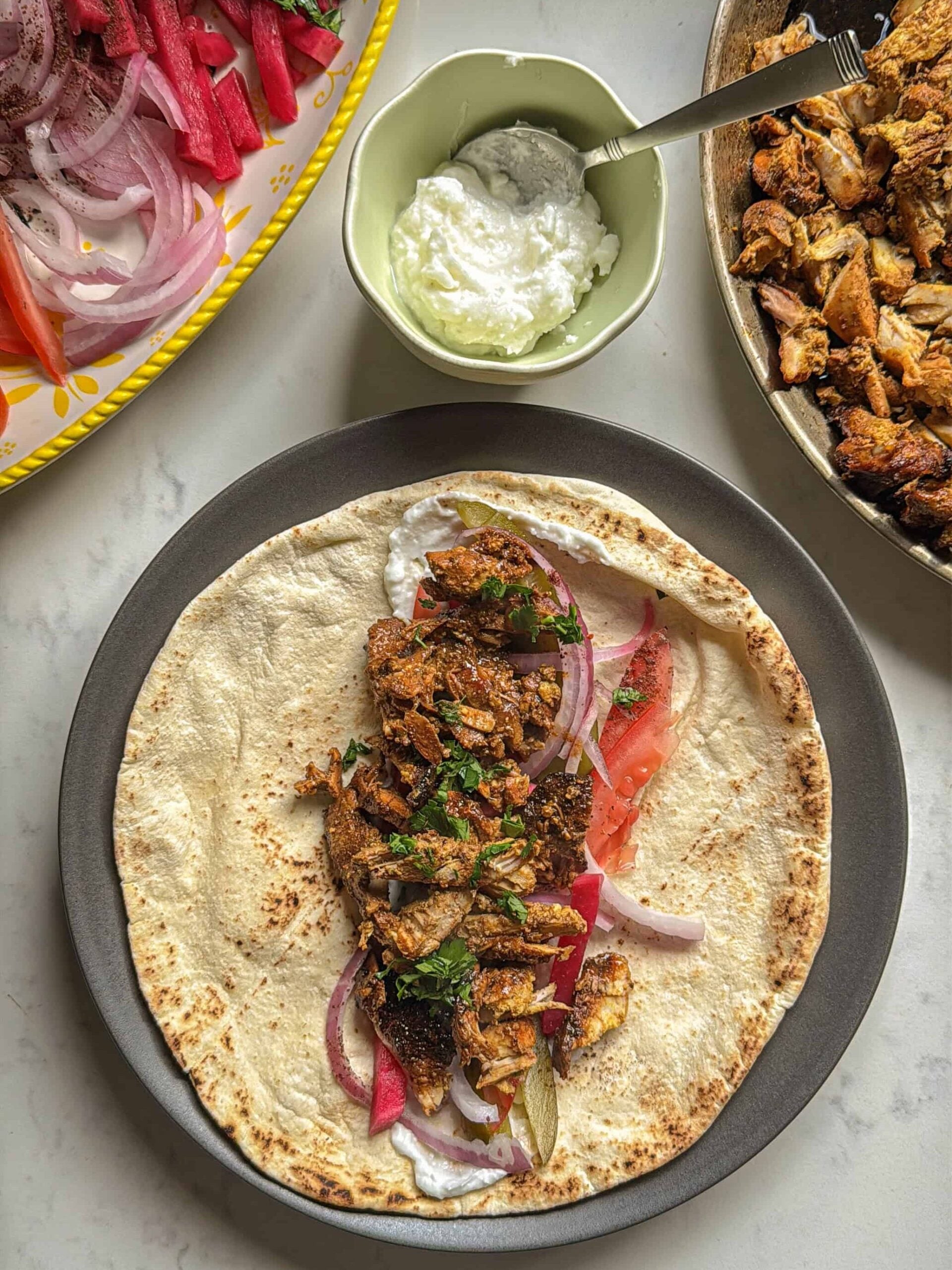 Chicken shawarma wrap laid open on flatbread with garlic sauce, pickled turnips, red onion, tomato, and fresh parsley
