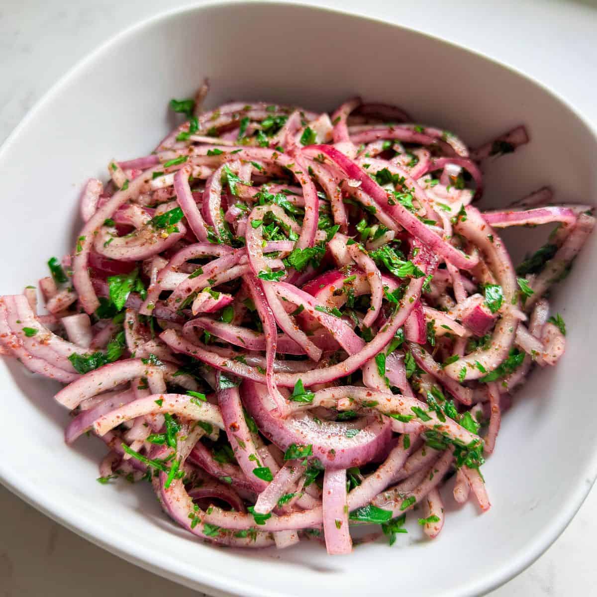 Close-up of sumac onion salad with parsley and olive oil in a white bowl