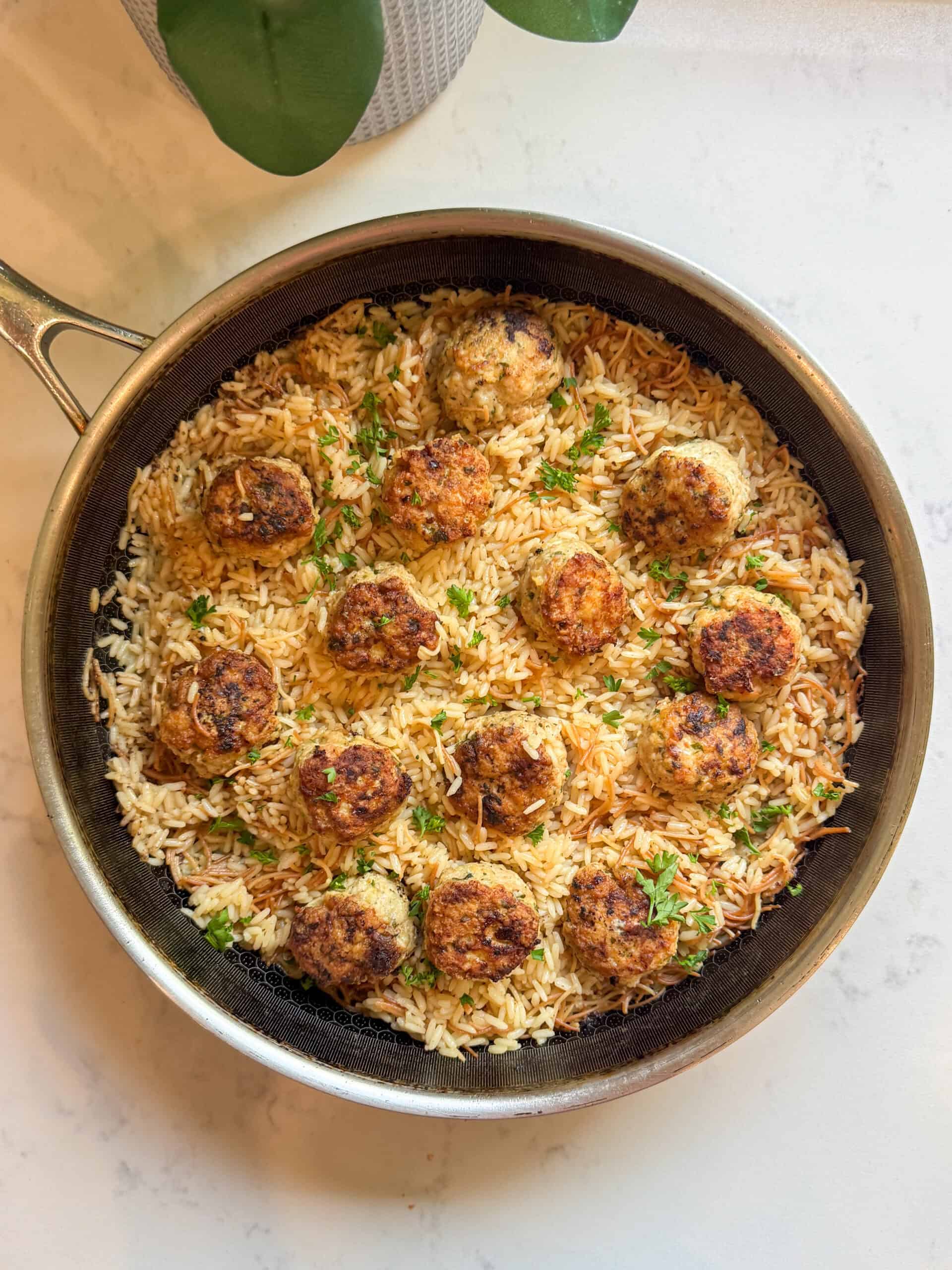 Overhead view of Greek chicken meatballs with rice pilaf in a skillet, garnished with fresh parsley