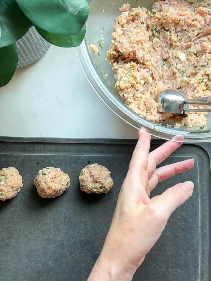 Hand rolling Greek chicken meatball mixture into balls on a baking sheet