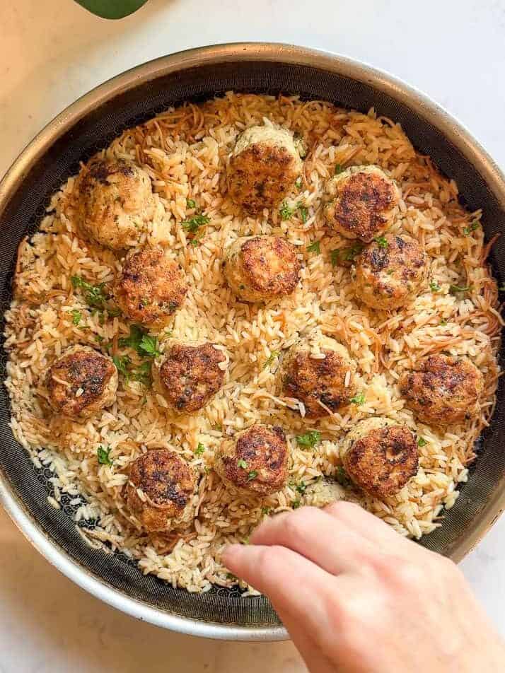 Finished Greek chicken meatballs and rice pilaf in a skillet, garnished with parsley