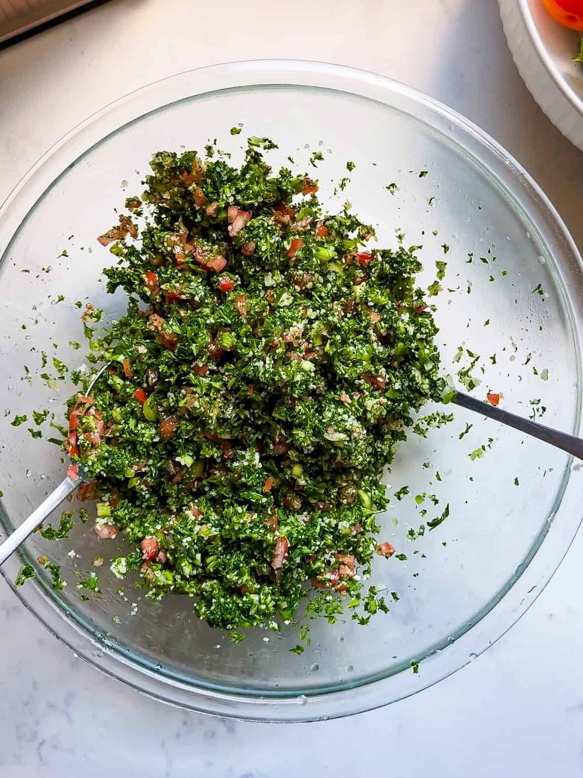 Tossing fresh Levantine tabbouleh with a spoon in a glass bowl