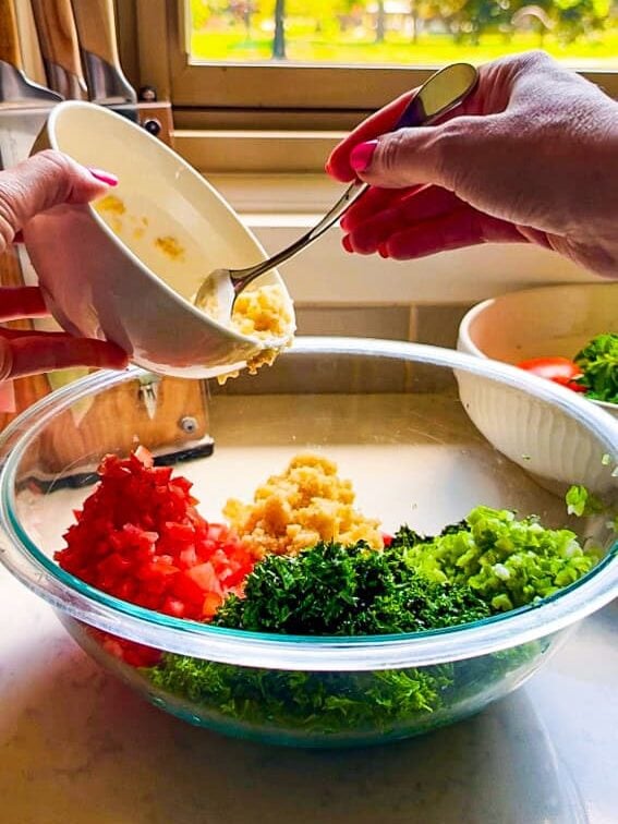 Adding hydrated bulgur to chopped parsley, tomato, and green onion for tabbouleh