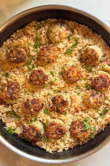Overhead view of Greek chicken meatballs with rice pilaf in a skillet, garnished with fresh parsley