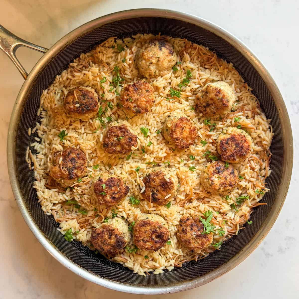 Overhead view of Greek chicken meatballs with rice pilaf in a skillet, garnished with fresh parsley