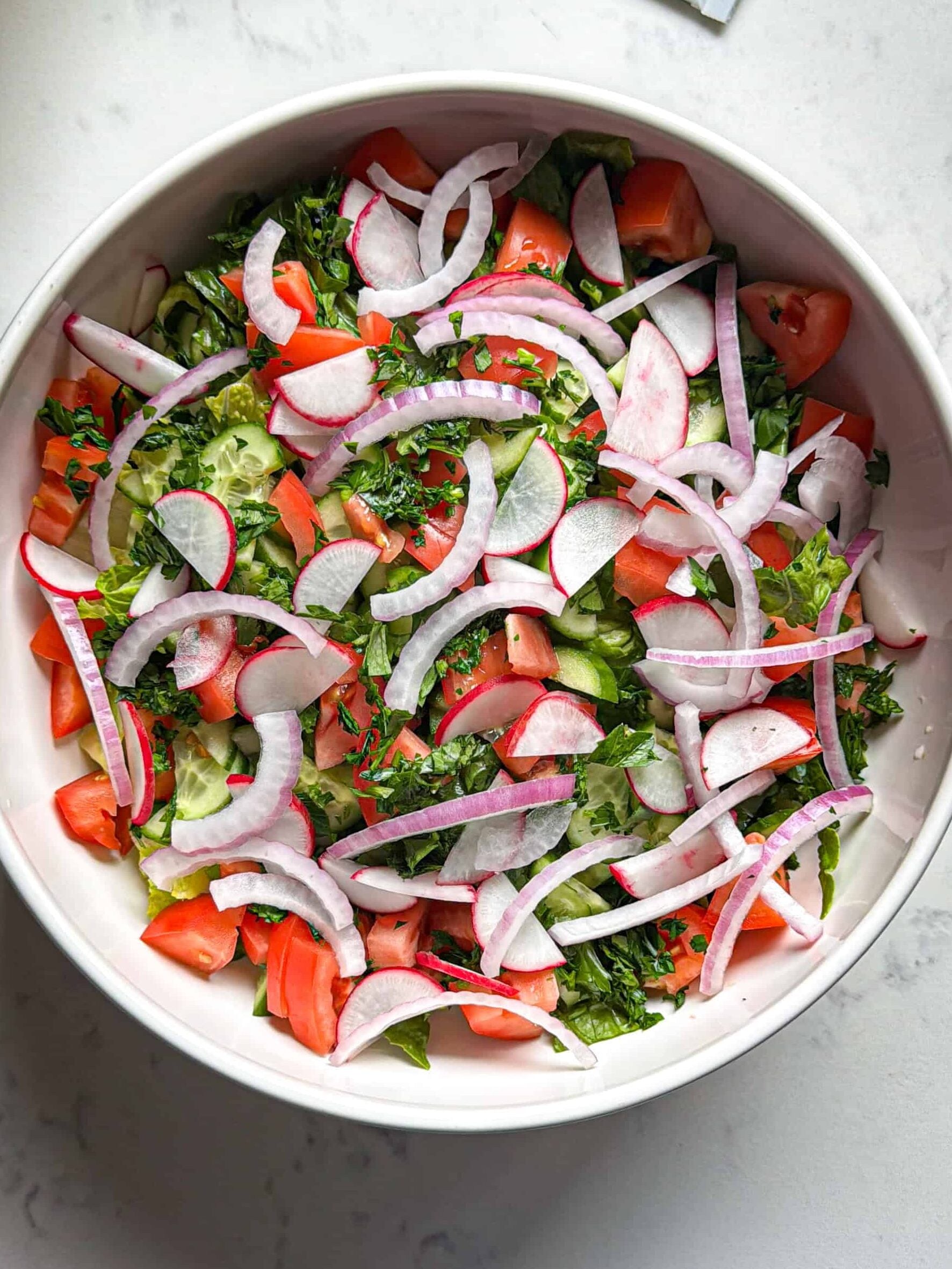 Chopped romaine, tomato, radish, and red onion in a bowl before adding fattoush dressing