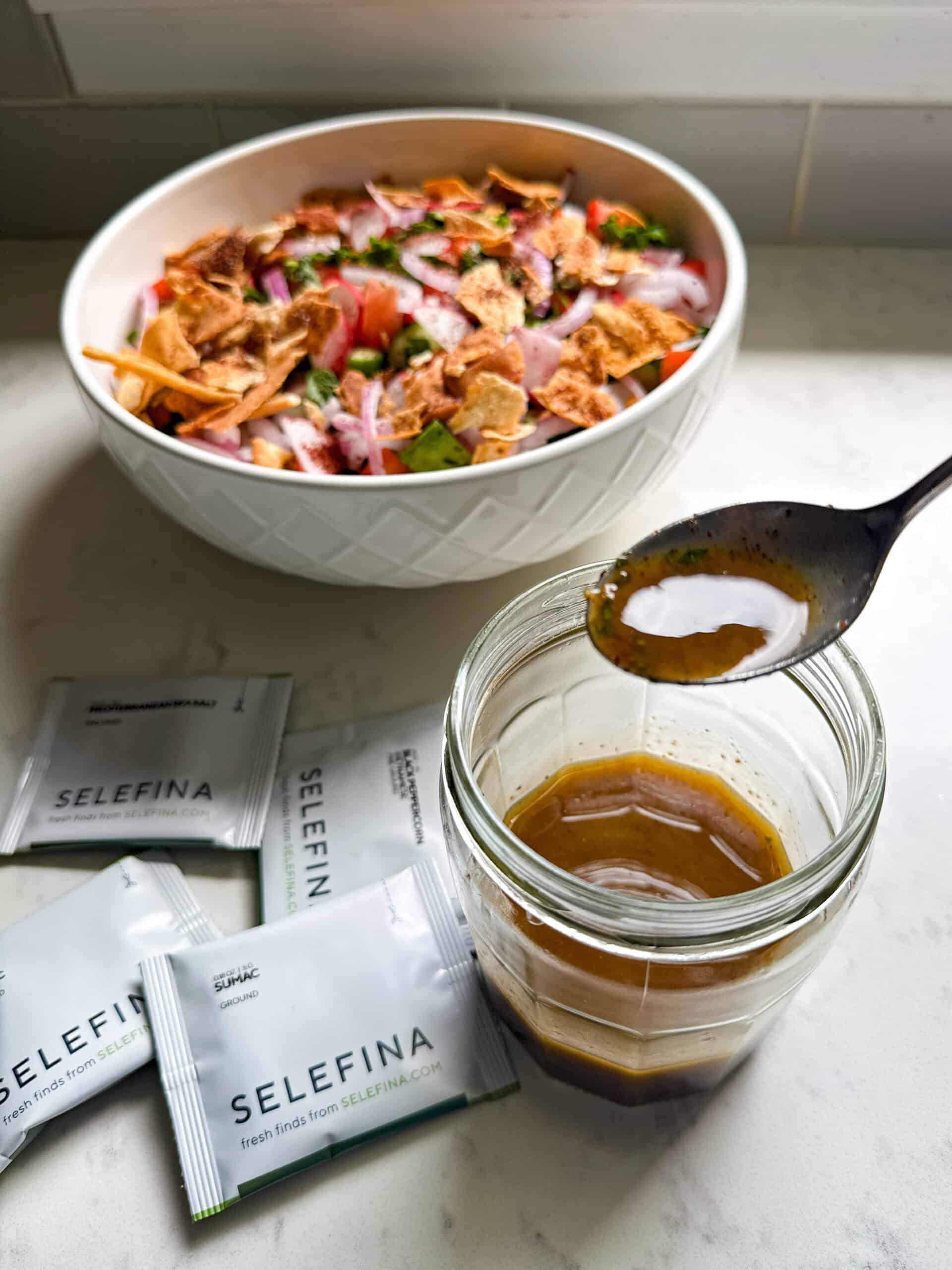 Finished fattoush salad beside a jar of sumac and pomegranate molasses dressing