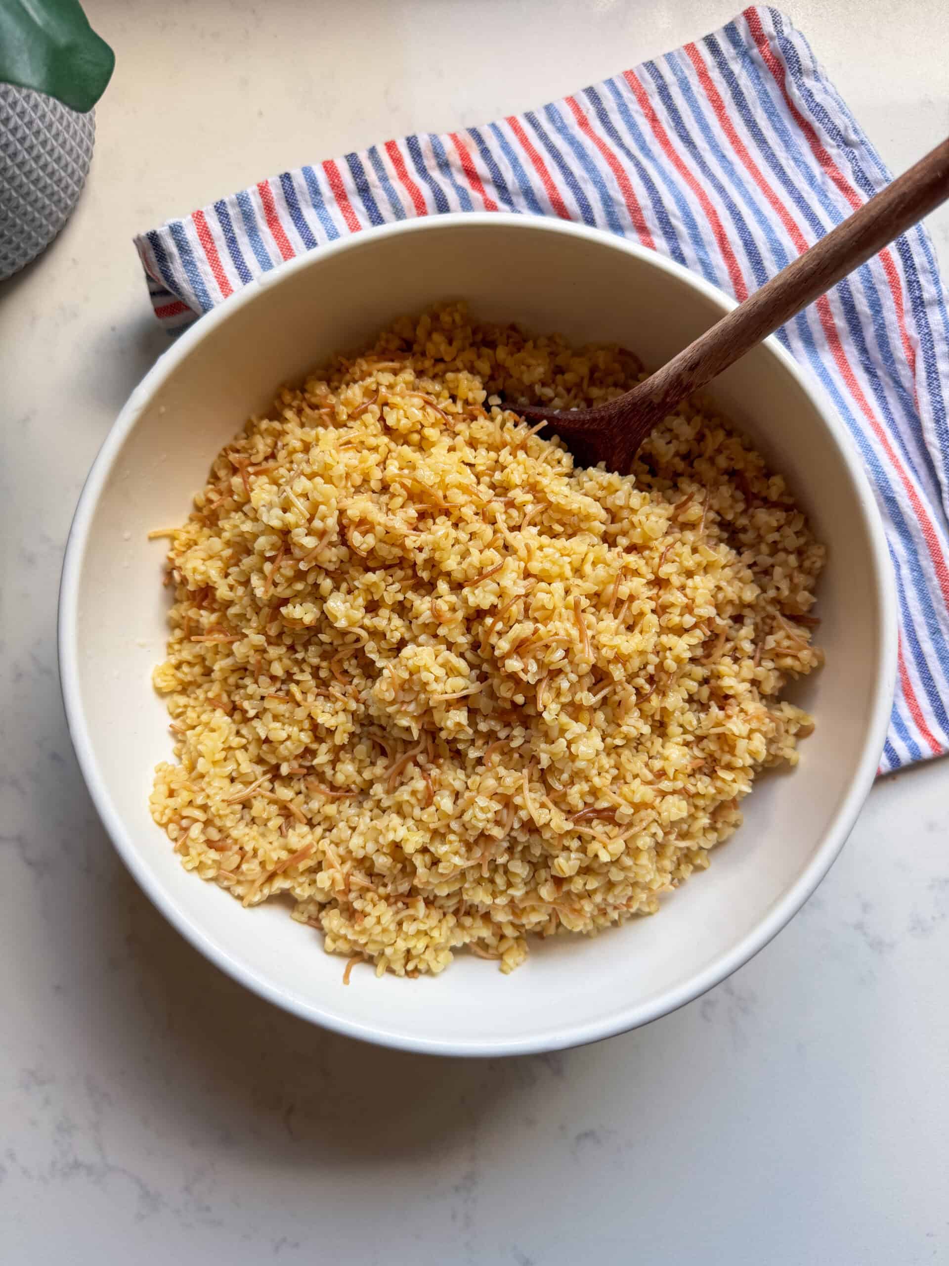 Overhead view of a bowl of golden bulgur pilaf with a striped kitchen towel