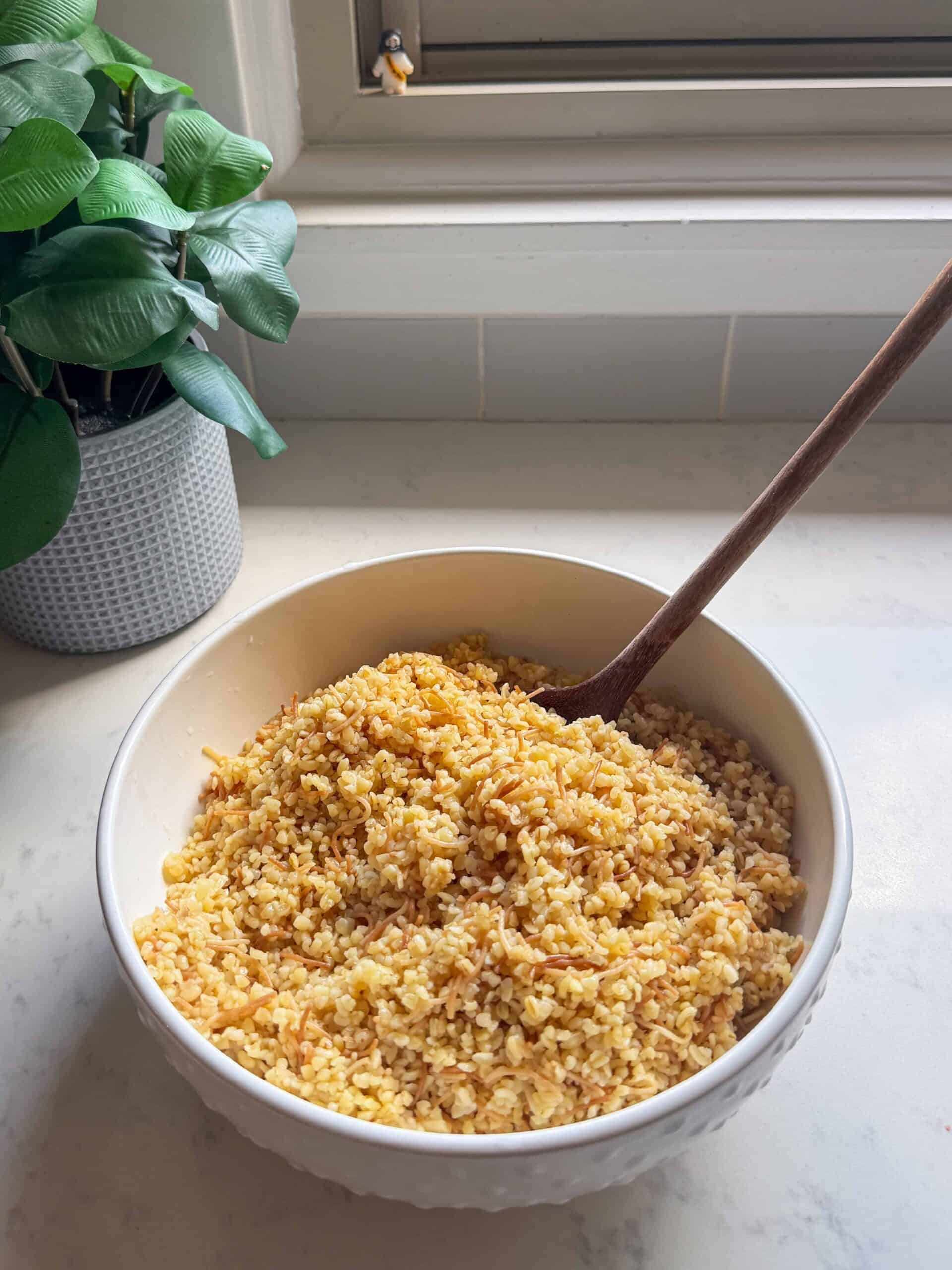Bowl of Armenian bulgur pilaf sitting on a marble counter with autumn trees visible outside
